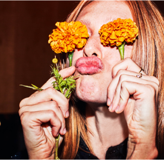 Woman holding two orange flowers over her eyes